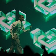 Stromae sur scène devant un fond d'écran vert. 