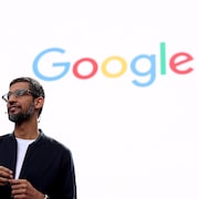 Le PDG de Google Sundar Pichai parle à une foule devant un écran orné du logo de Google. 