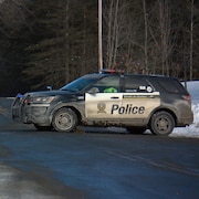 Un VUS de la Sûreté du Québec placé en travers d'une route dans un secteur boisé, en hiver.