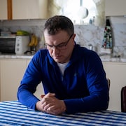 Sylvain Dufour est assis dans la cuisine de sa mère. Il regarde ses mains qui sont croisées.
