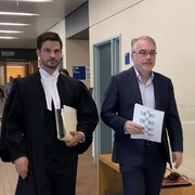Les deux hommes marchent dans un corridor du palais de justice.  Le psychiatre est vêtu d'un complet alors que le procureur porte sa toge.  Les deux tiennent des documents dans leur main.