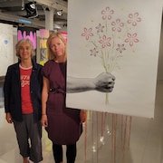 Deux femmes se tiennent à côté d'une affiche sur laquelle on voit une main tenir un bouquet de fleurs.