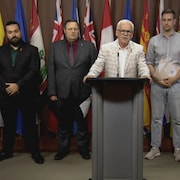 Six hommes se tiennent debout devant un pupitre lors d'une conférence de presse.