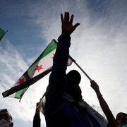 Des gens qui portent des drapeaux syriens manifestent.
