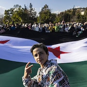 Un jeune garçon fait le signe de la victoire devant une foule qui brandit le drapeau de la révolution.