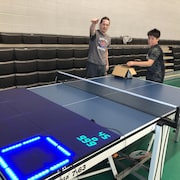 Éric Boily parle activement à un jeune qui s'apprête à lancer une balle de ping-pong. 