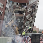 Une pelle mécanique démolit un bâtiment endommagé par un tremblement de terre.