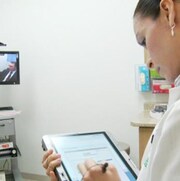 Une professionnelle de la santé prend des notes face à un écran où apparaît un patient.
