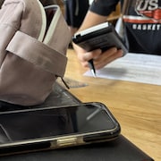 Un élève assis à un bureau avec une calculatrice dans les mains et un téléphone sur son bureau.