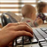 Gros plan d'une main sur un clavier, avec des enfants en arrière-plan.