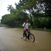 Un homme roule en vélo sur une voie inondée.