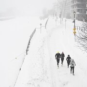 Des joggeurs courent pendant une tempête de neige dans une rue de Montréal. 