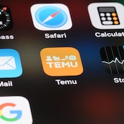 Un écran de téléphone montre plusieurs applications mobiles, dont Temu, au centre.