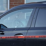 Une voiture sur laquelle on remarque des impacts de balles dans la vitre côté conducteur.