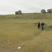 Deux hommes se tiennent dans un terrain vague couvert d'herbe en bordure d'une route.