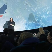 Une femme parle à des spectateurs devant un écran en forme de dôme.