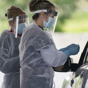 Deux infirmières, dont une tient un écouvillon, discutent avec un automobiliste.