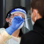 Une infirmière s'approche pour récolter un échantillon dans la narine d'une personne.