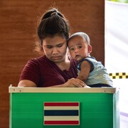 Une mère tient son enfant dans ses bras et dépose un bulletin de vote.