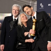 Elliott Broidy, Sylvia Plachy et Adrien Brody, qui tient un trophée en souriant, la tête penchée.