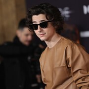 L'acteur vêtu de cuir beige avec des lunettes de soleil opaques.