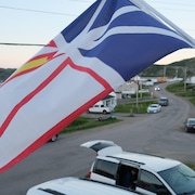 Le drapeau provincial de Terre-Neuve-et-Labrador flotte au vent au-dessus d'une route qui traverse un village.