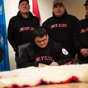 Duane Smith signe un document. Quatre personnes sont debout derrière, le 24 novembre 2021, à Inuvik, aux Territoires du Nord-Ouest.
