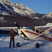 Une personne debout à côté d'un avion en hiver dans les montagnes, en décembre 1978.