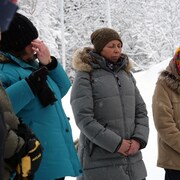 Quatre personnes debout dehors, en hiver, avec tuques et manteaux.