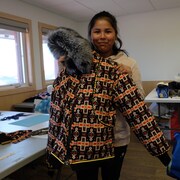 Jeune fille qui tient devant elle un parka avec accent de fourrure en août 2022 dans la communauté de Behchoko, aux Territoires du Nord-Ouest.