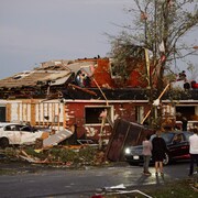 Plusieurs personnes sont debout dans la rue ou sur le toit d'une maison en ruines.