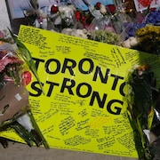 Une carte jaune « Toronto Strong »  et couverte de nombreux messages, déposée au milieu des fleurs sur les lieux de l'attaque mortelle à Toronto.