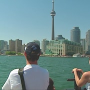 Centre-ville de Toronto avec tour du CN, eaux du lac Ontario et touristes sur le traversier en avant-plan.