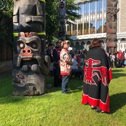 Des représentants de Premières Nations de l'île de Vancouver s'adressent au public au pied de totems.