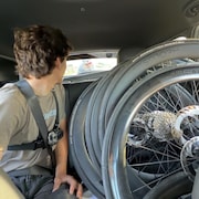 Un cycliste suit de pr&egrave;s une voiture remplie de roues de v&eacute;lo.