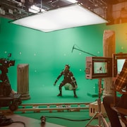 Un homme portant une combinaison recouverte de capteurs est filmé par une équipe de tournage dans un studio avec des écrans verts. 