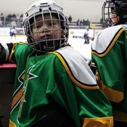 De jeunes joueurs de hockey filmés de près sur le banc pendant qu'on voit l'image floutée d'autres joueurs sur la patinoire.