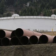 Des tuyaux devant servir à transporter du pétrole avec, en arrière-plan, un réservoir dans la région de Kamloops, en Colombie-Britannique.