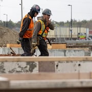 Deux jeunes hommes équipés des casques, de vestes et de gants de travail discutent en marchant.