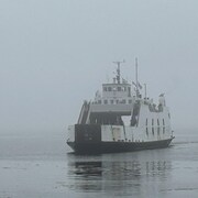 Un traversier navigue sur le fleuve embrumé.