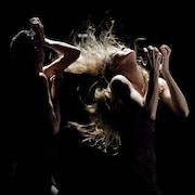 Deux danseurs et danseuses dans le noir, illuminés partiellement. 