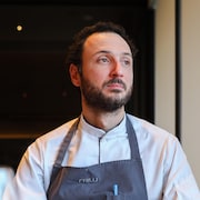 Le chef étoilé Jean-Vincent Troiano assis dans une table de son restaurant et regarde vers la fenêtre. 