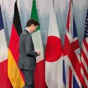 Justin Trudeau, debout devant les sept drapeaux des pays du G7. 