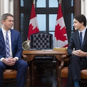 Justin Trudeau et Andrew Scheeer, assis, se regardent. 