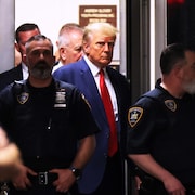 L'ancien président américain Donald Trump escorté par des policiers.