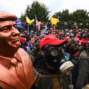 Un partisan de Donald Trump porte un masque à gaz et tient un buste de l'ancien président durant l'assaut du Capitole.