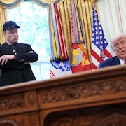 Donald Trump assis dans le bureau ovale; Elon Musk est debout, les bras croisés.