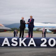 Donald Trump et Vladimir Poutine se serrent la main sur une scène, devant Air Force One.