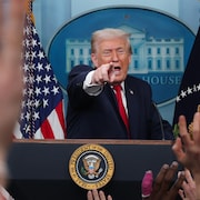 Donald Trump au lutrin de la salle de presse de la Maison-Blanche, montrant quelqu'un du doigt, alors que plusieurs journalistes lèvent la main.