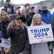 Deux femmes portent une pancarte sur laquelle on peut lire Trump 2024. Une autre femme a le poing levé et une casquette "Trump 2024. Save America". 